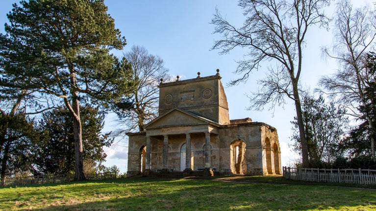 The cream stone Temple of Friendship at Stowe in Buckinghamshire surrounded by greenery and trees
